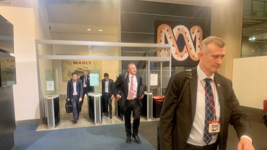 Several men in suits walking in the ABC building foyer.
