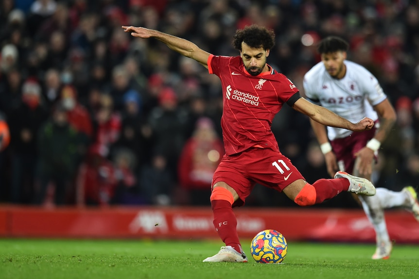 Liverpool's Mohamed Salah looks down at the ball as he swings his leg through in the action of taking a penalty kick.