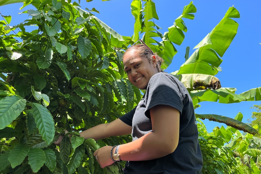 Women smiles at camera whilst handling a coffee bush