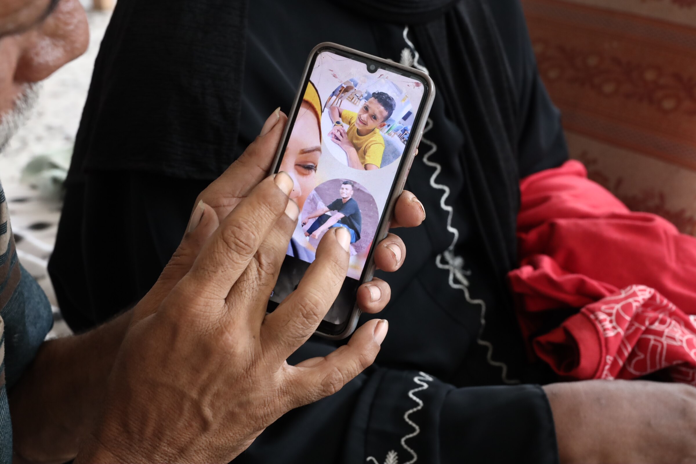 A hand tapping on the screen of a phone showing a picture of a young boy.