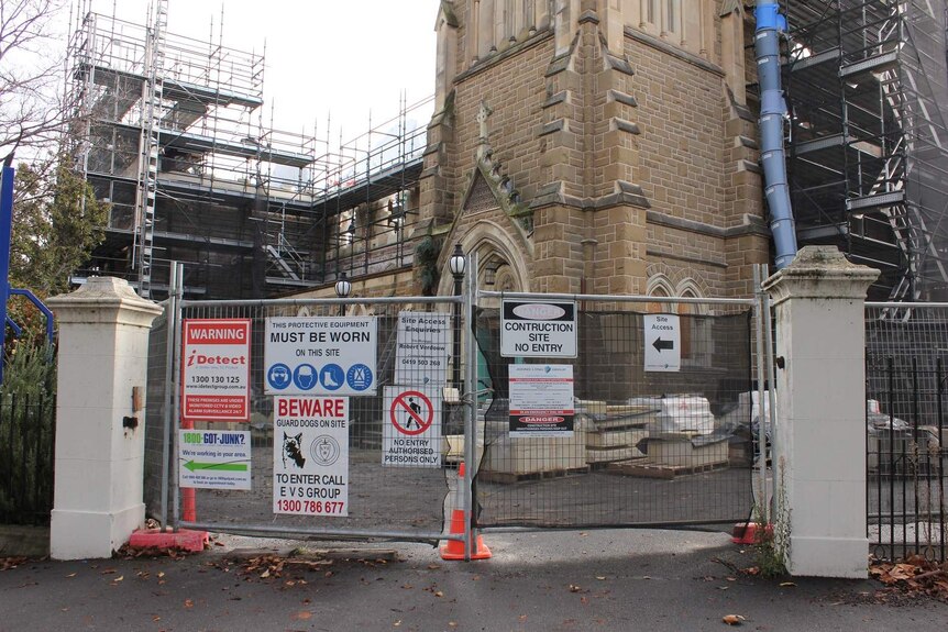 The exterior of a church with construction scaffolding and gates surrounding it.