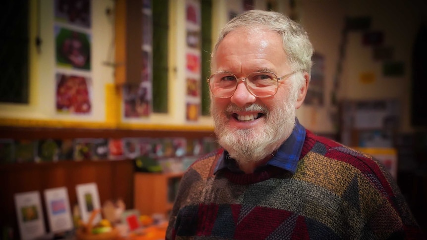 A grey-haired man in a colourful jumper smiles at the camera.