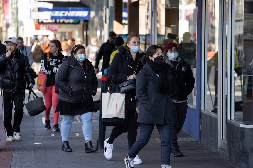 People walking past shops on a city street, some are wearing face masks