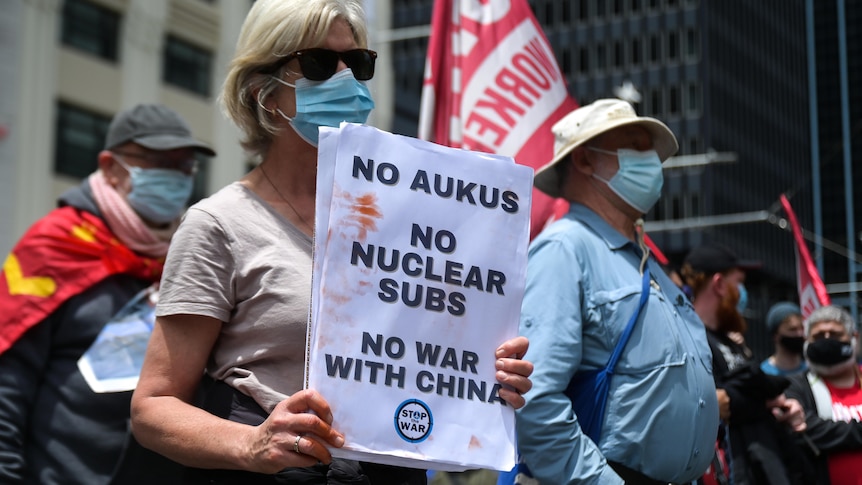 woman holding placard saying 'No AUKUS, no nuclear subs, no war with China'