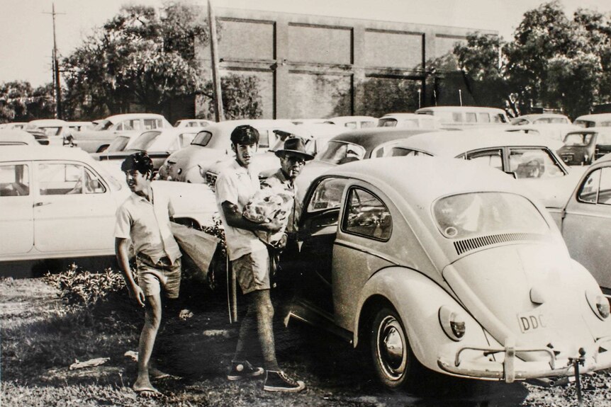 A black and white photo from 1966 of a man and his two sons loading meat into a car outside Homebush abattoir.