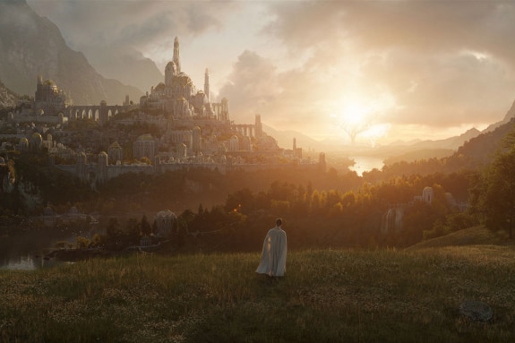 A figure in a long white coat stands in a field, looking up towards a castle in the distance.