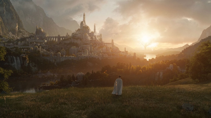 A figure in a long white coat stands in a field, looking up towards a castle in the distance.