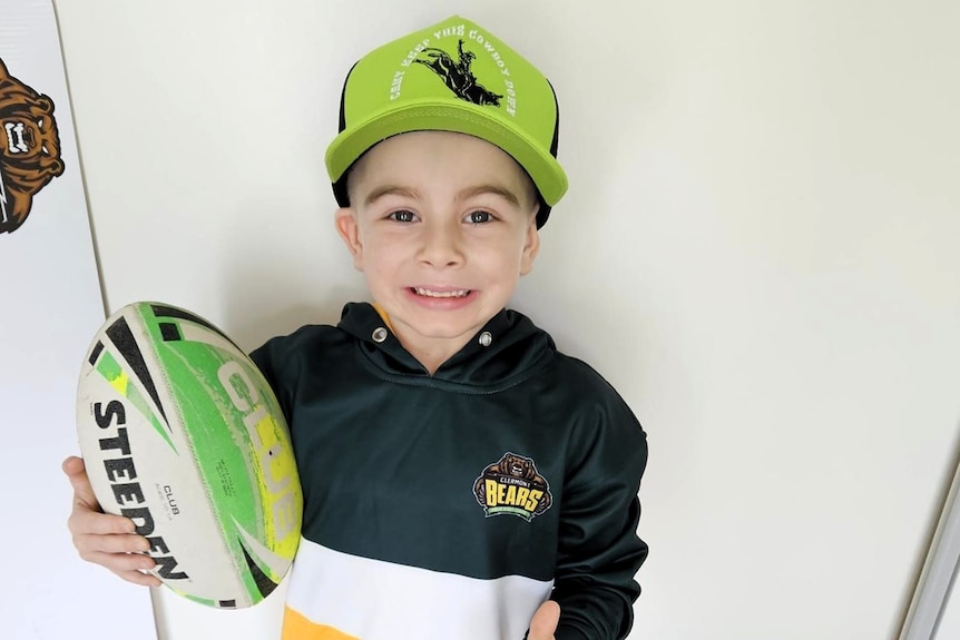 A young boy in yellow and green football colours for the Clermont Bears, holding a rugby league ball.