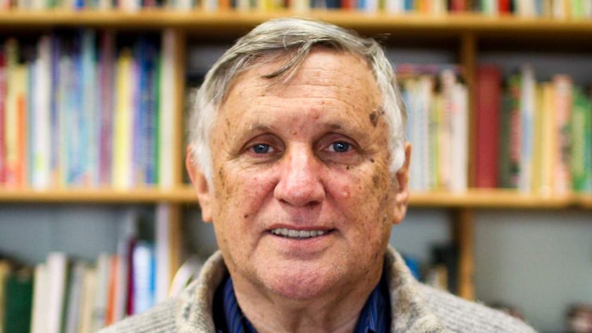 John Marsden stands in front of a bookshelf as he smiles at the camera.
