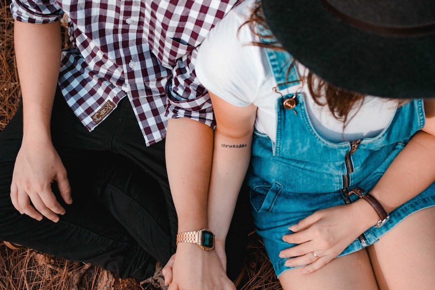 A couple holding hands, sitting close together, their faces are not seen