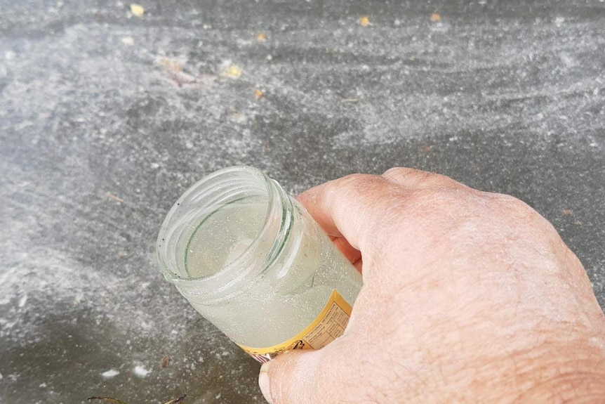 A hand holds a bottle of murky-coloured water taken from a river