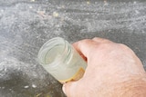 A hand holds a bottle of murky-coloured water taken from a river