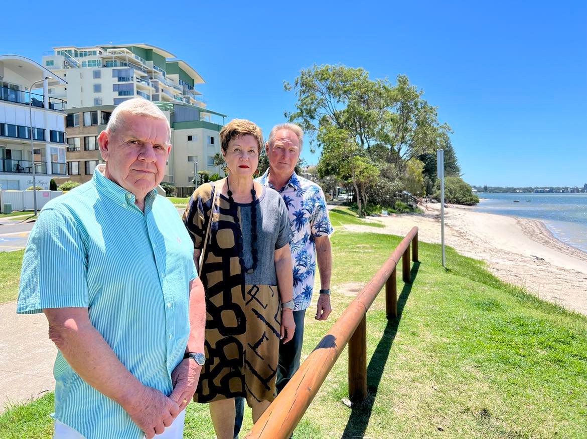 Man in blue shirt, woman in dress and man in patterned shirt looking at Golden beach foreshore