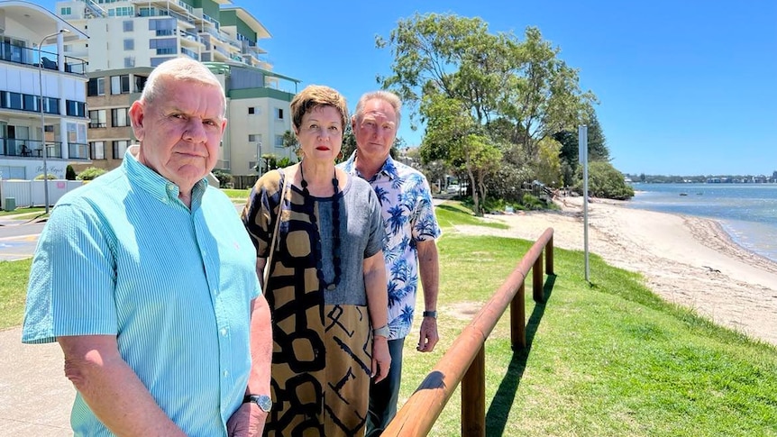Man in blue shirt, woman in dress and man in patterned shirt looking at Golden beach foreshore.