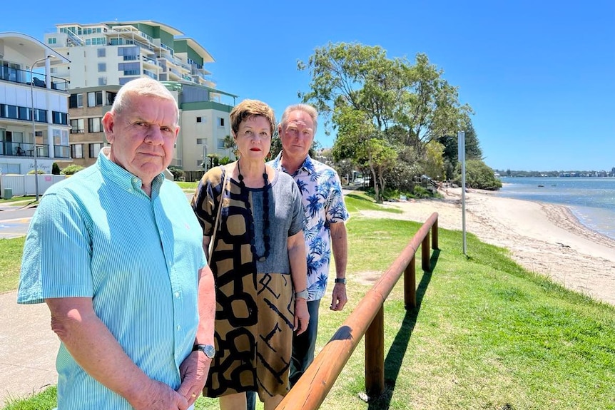 Man in blue shirt, woman in dress and man in patterned shirt looking at Golden beach foreshore