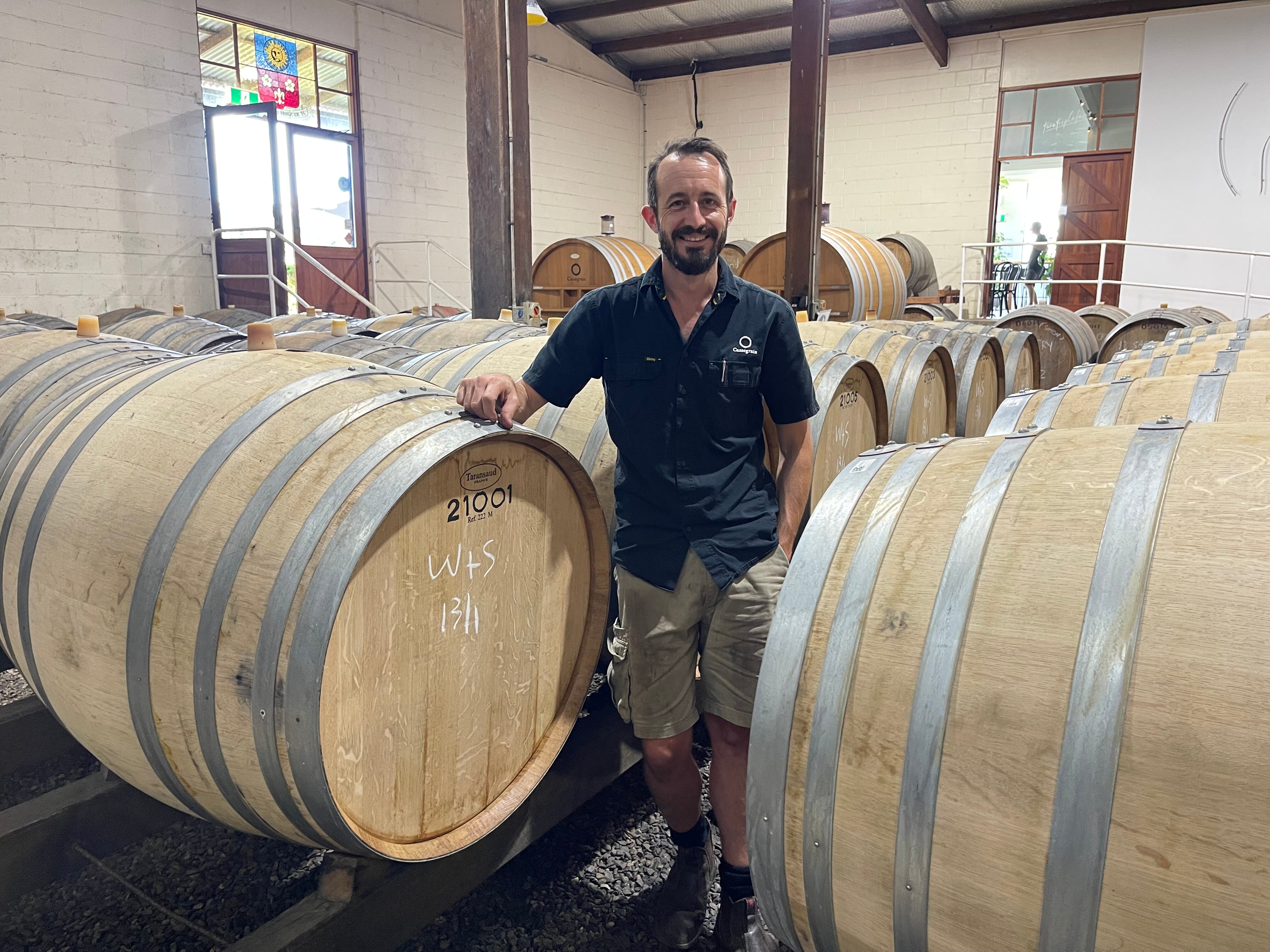 A man standing among barrels of wine.