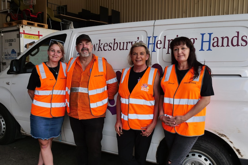 Four people in orange vests smile in front of a van