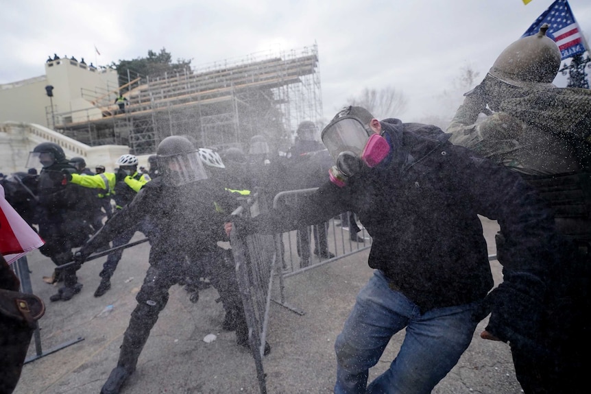 Trump supporters try to break through a police barrier as tear gas fills the air.