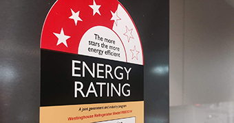 Close up of energy star rating sticker on chrome refrigerator, microwave and kettle in background.