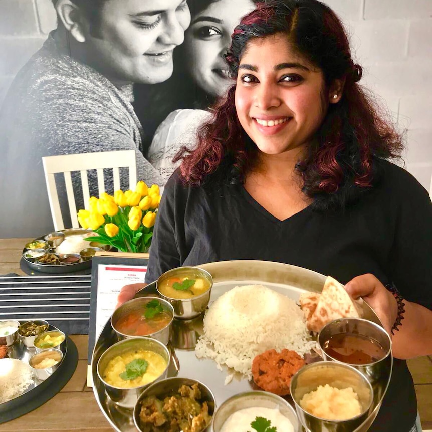 Preethi holds a huge dish filled with various curries, chutneys, rice and naan.