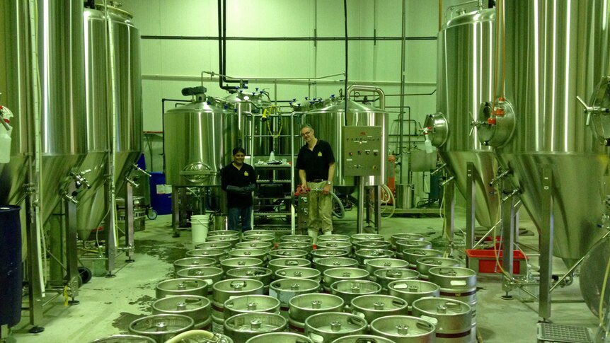 Two brewers working in a brewery with lots of kegs and tanks.