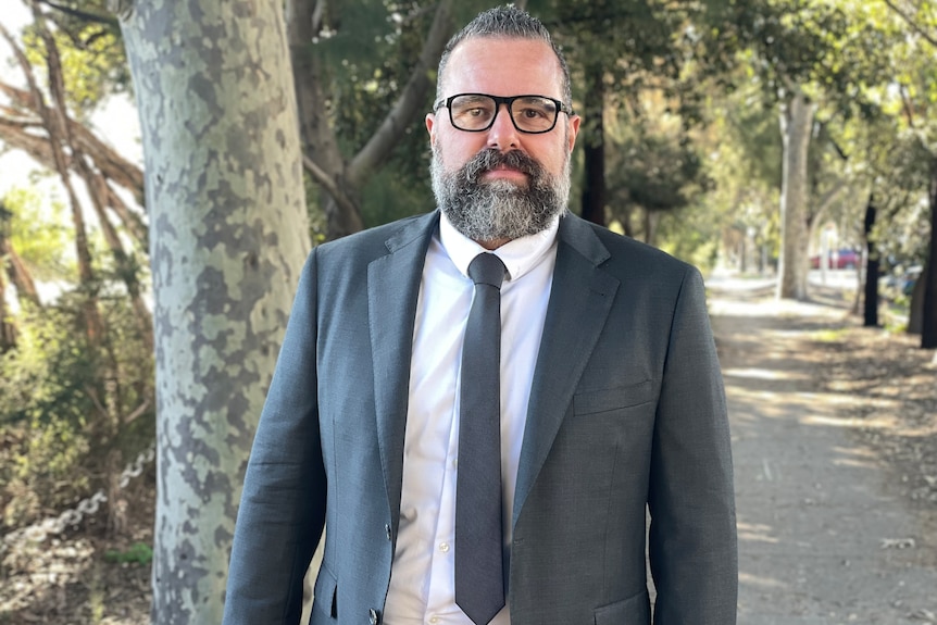 A man wearing glasses and a grey suit standing in a park.