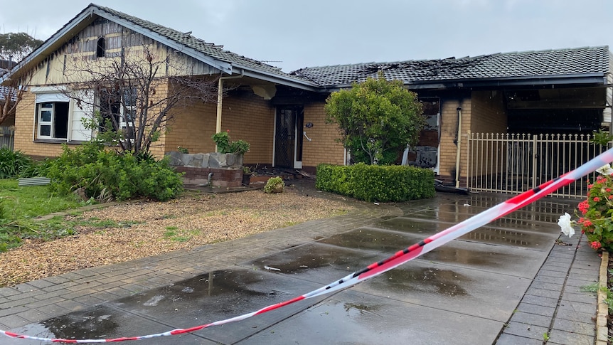 A house with fire damage and red and white tape strung across the foreground