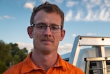 A man wearing an orange shirt stands next to a ute.