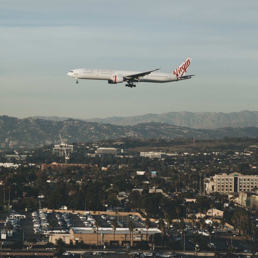 A Virgin Australia plane flies over a small city