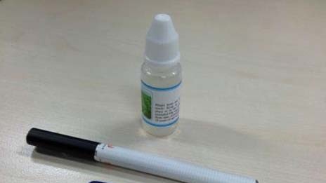An e-cigarette sits next to a vial of nicotine