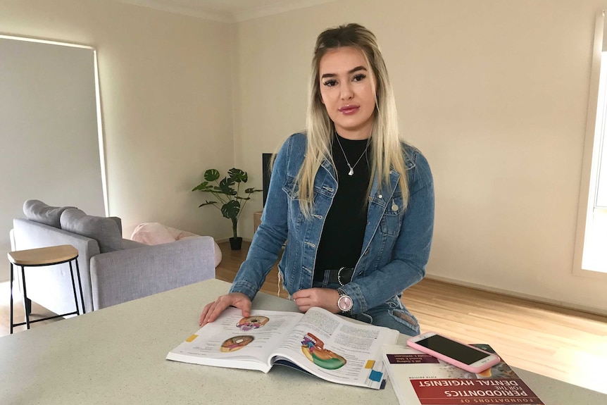 A woman stands at a kitchen counter with dental studies books open in front of her.