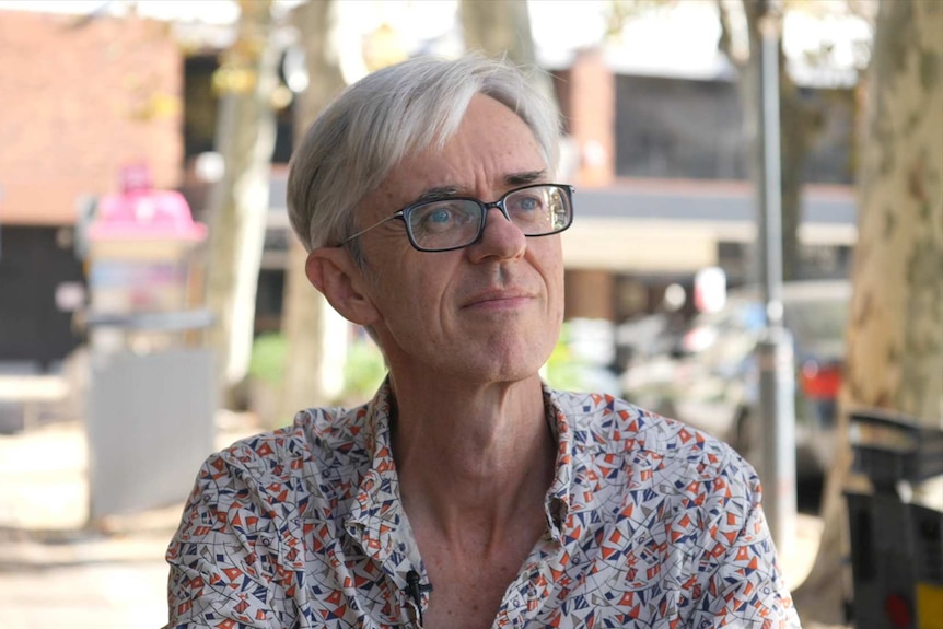A man with black rimmed spectacles, grey hair and a colourful shirt in a street