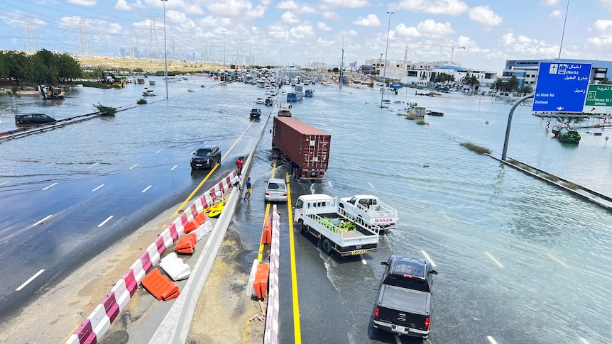 A wide road covered in water with cars and trucks stuck in the middle.