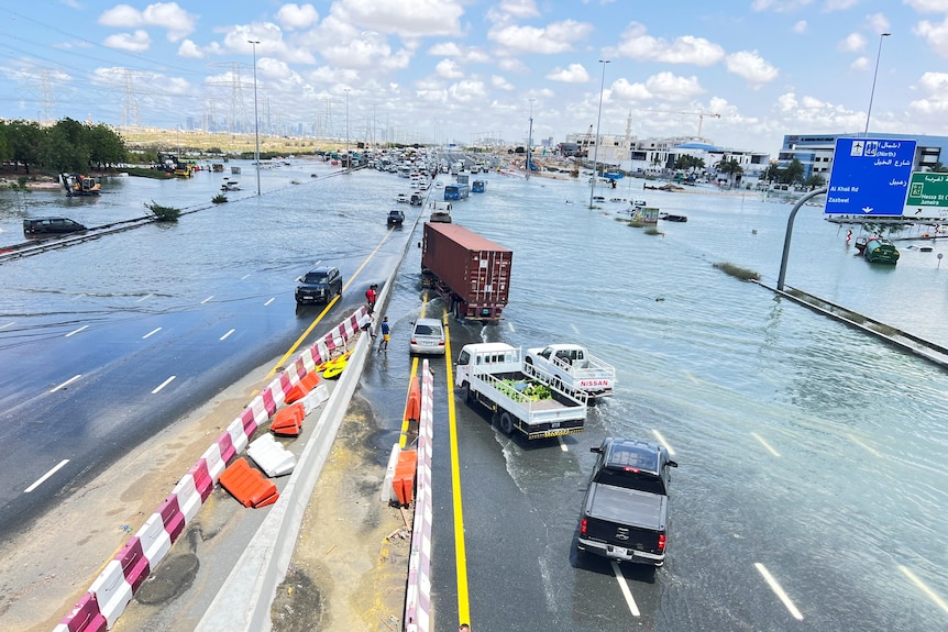 A wide road covered in water with cars and trucks stuck in the middle.