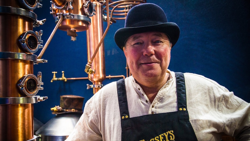 Man in bowler hat standing in front of a gin still