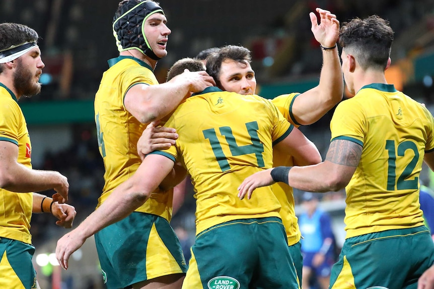 A collection of happy Wallabies players converge to high-five and hug each other.