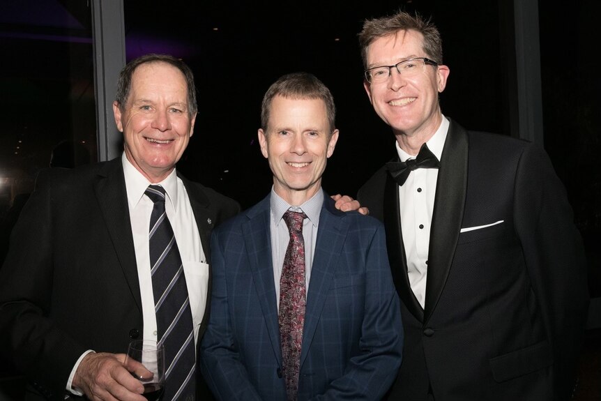 a photo of three men in suits smiling at camera 
