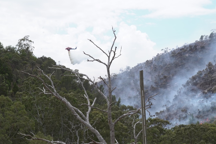 A red helicopter drops water on hills with smoke