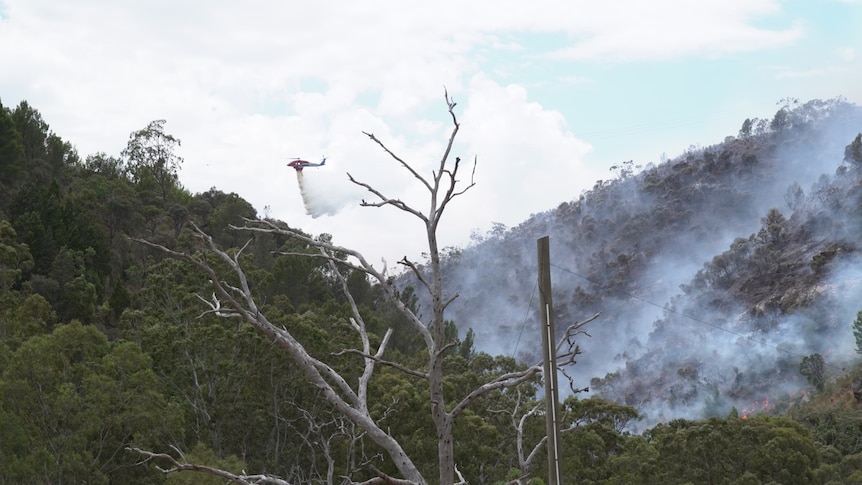 A red helicopter drops water on hills with smoke