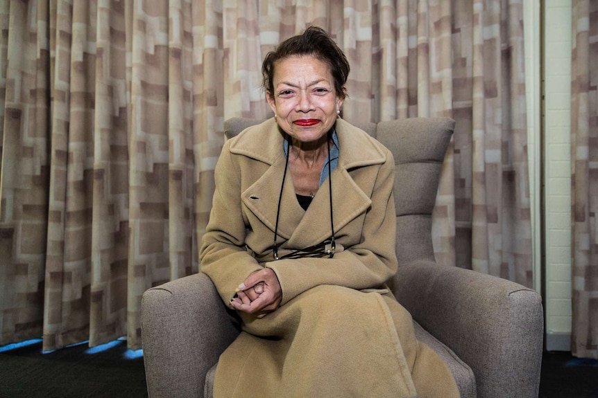 A woman in an overcoat sits in an armchair.