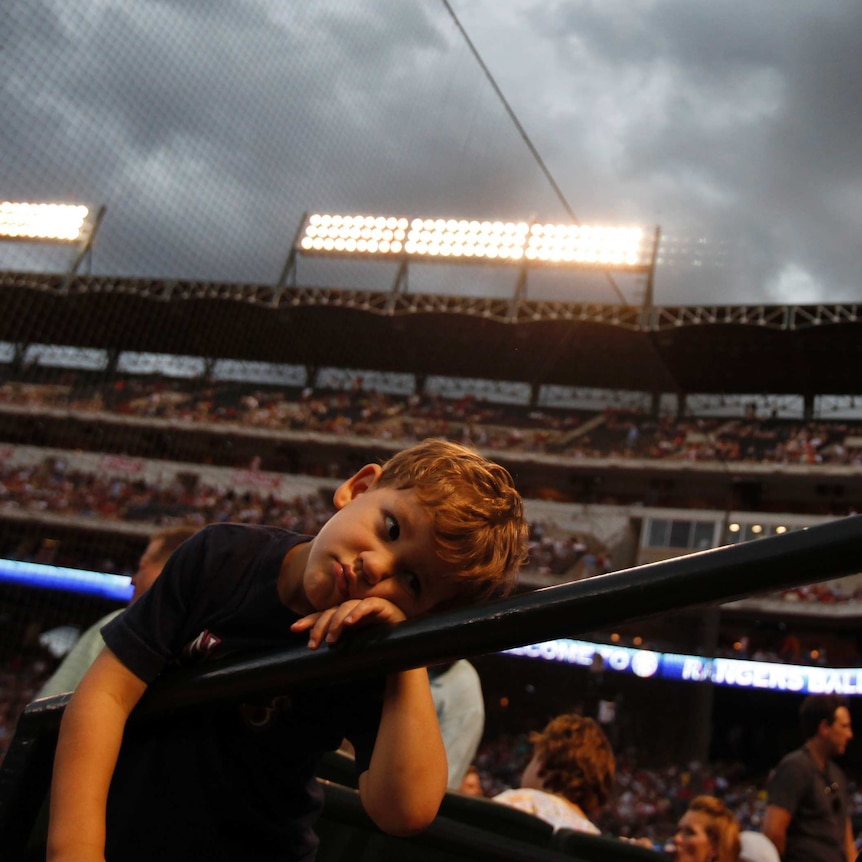 A boy rests his head on a railing as he waits during a rain delay before the start of American League MLB baseball game.