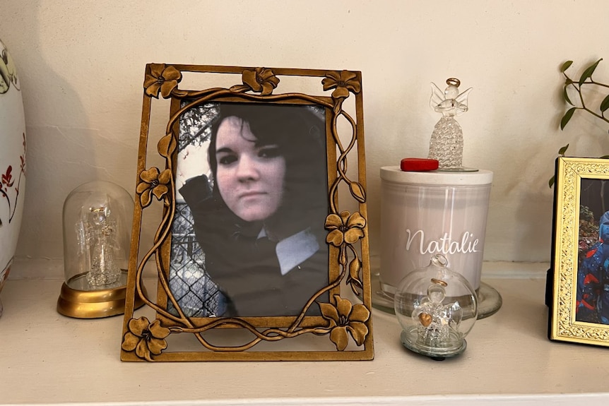 A framed photograph of Natalie Russell next to a candle with the word Natalie on it. 