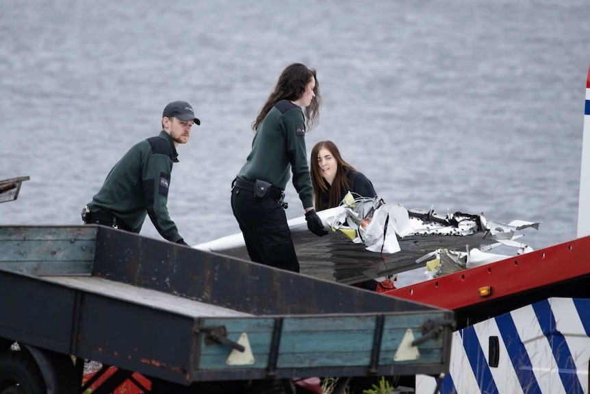 Three emergency service personnel lift a piece of aeroplane wreckage on to a truck.