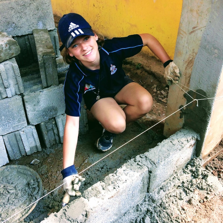 A young high school student in her uniform building a brick wall.