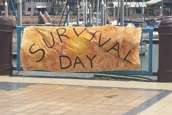 A banner with the words survival day written on it hangs on a fence on a sidewalk.