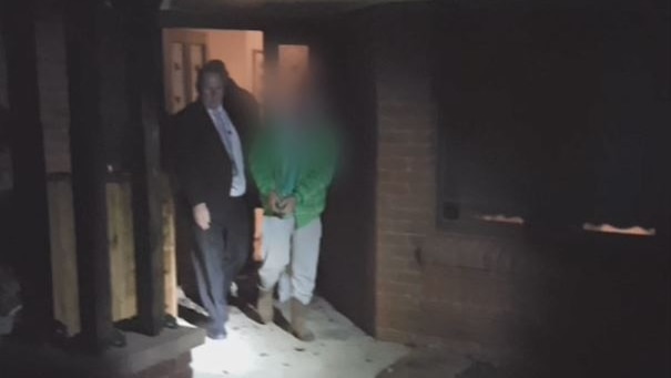A man is led out of his home in handcuffs.