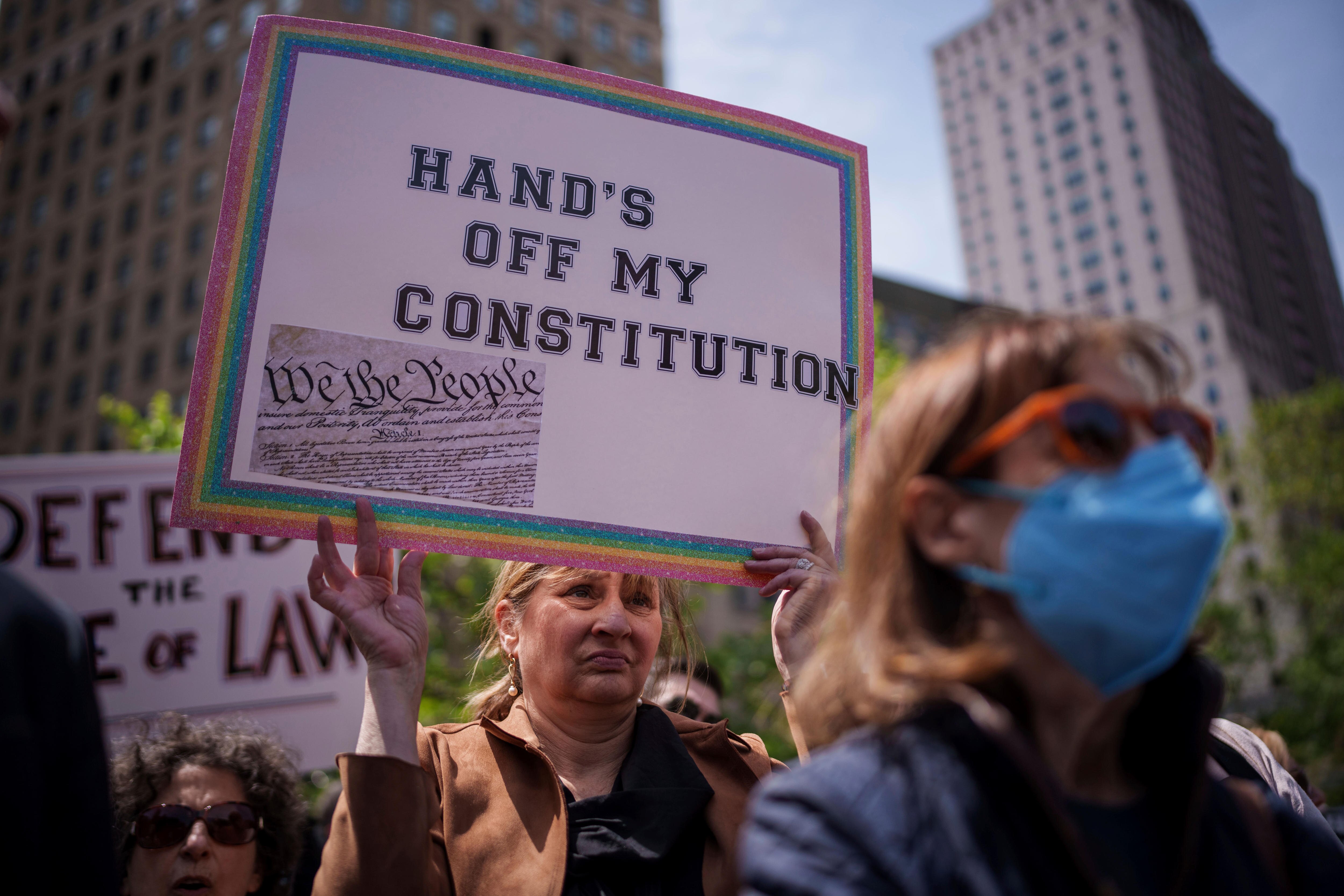 A woman frowning holds up a sign saying 'hand's off my constituion 