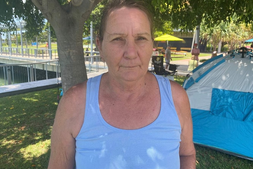 A woman stands in a park under a tree and looks at the camera