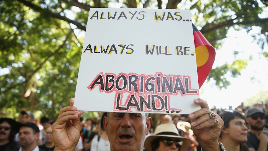 A man holds a sign that says 'Always was.. Always will be Aboriginal Land.'