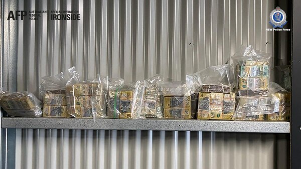 Wads of cash sitting on a shelf mounted on a corrugated iron wall.